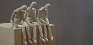 Three wooden figures sitting with heads down, representing fatigue or emotional exhaustion